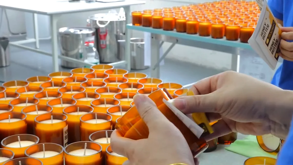 A brand label being applied by hand to an amber candle jar in the factory